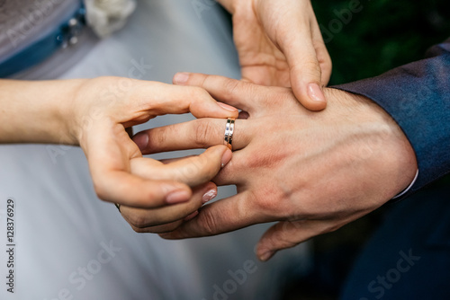 Bride wears the ring on the finger of the groom. Cropped image