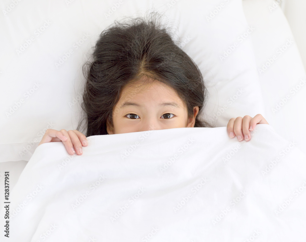 Portrait of happy young Asian girl lying on the bed after waking up and
