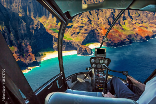 Helicopter cockpit flies in Na Pali coast, Kauai, Hawaii, United States, with pilot arm and control board inside the cabin.