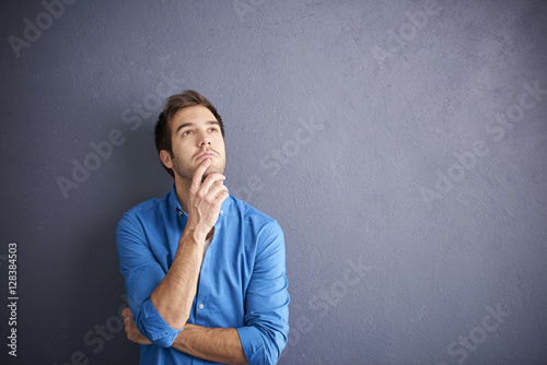 Young man portrait with copy space. Shot of a handsome man relaxing in front of a grey wall while looking at camera and smiling. 