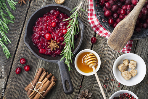 Fresh homemade cranberry sauce in a pan on dark wooden background with scattering of ripe berries. photo