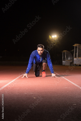 Plakat Runner, sprinter start position, looking at camera. Dark night.
