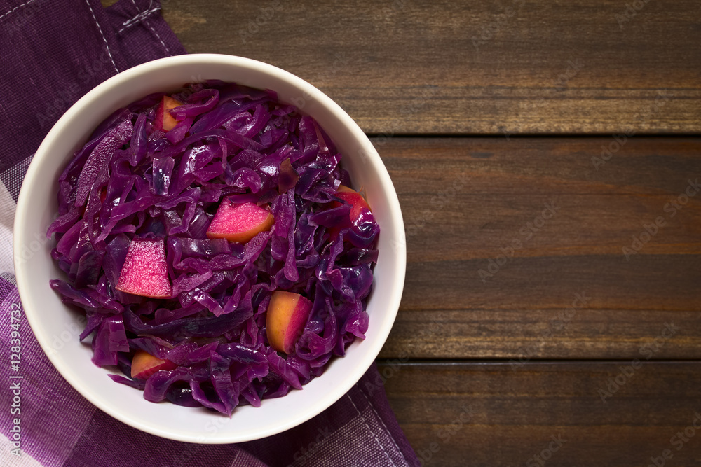 Braised red cabbage with apple in bowl, photographed overhead on dark wood with natural light (Selective Focus, Focus on the top of the dish) Braised red cabbage with apple in bowl, photographed overhead on dark wood with natural light (Selective Focus, Focus on the top of the dish)