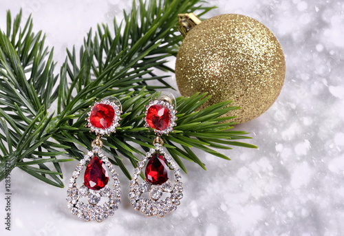earrings with red stones on a branch of a Christmas tree with a ball on an abstract background