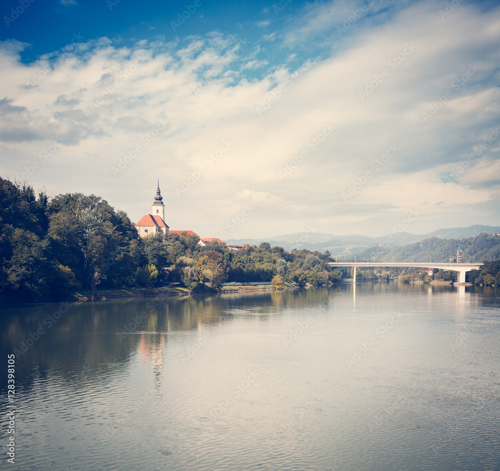 Old Church on River Bank on Mountains Background. Typical Landscape in Slovenia. St. Joseph Church in Maribor on Drava River. Popular Touristic Destination in Slovenia, Europe. Toned Photo.