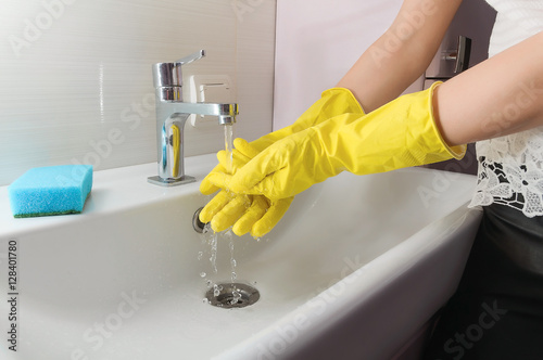 Fototapeta Naklejka Na Ścianę i Meble -  Woman hand in yellow rubber glove in water stream