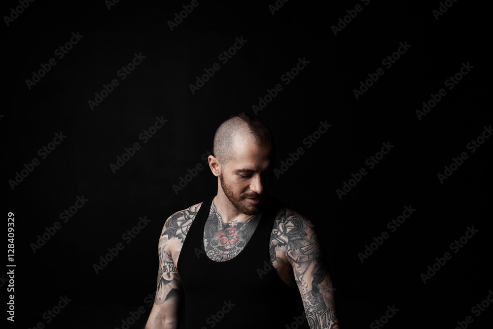 Brutal european man in black shirt with short hair stay and look down on black neutral background. 30 years guy with short beard in dreams. Fighter before battle.
