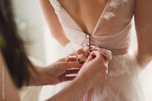 Closeup of bridesmaid tying bow on bride's dress