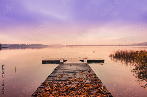 Wooden pier with leaves on the quiet lake at sunrise in autumn
