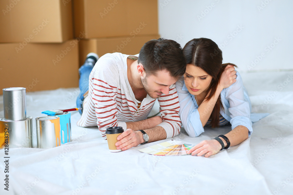 Couple choosing paint colour from swatch for new home lying on wooden floor Couple choosing paint colour from swatch for new home lying on wooden floor