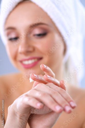 Beautiful young woman applying a creme her face isolated on gray background