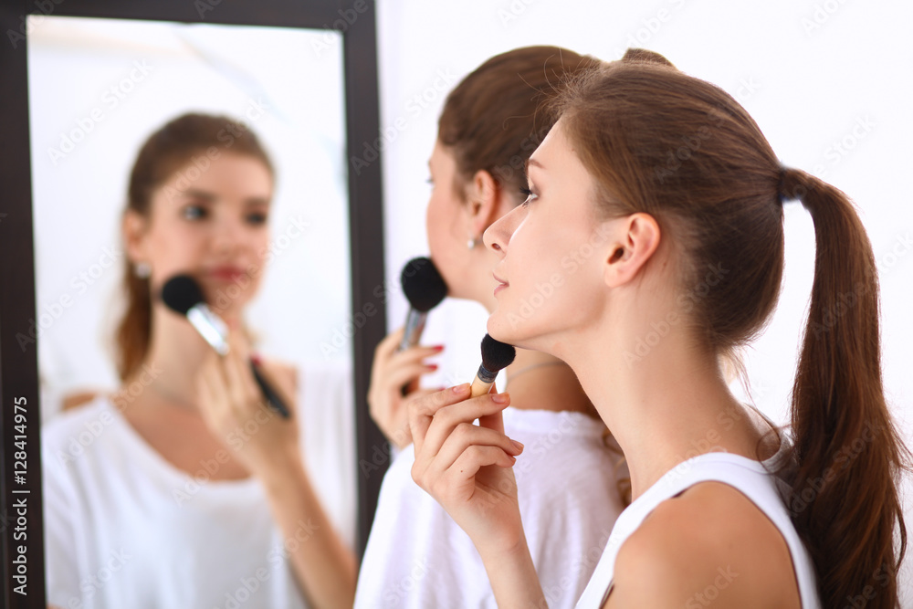 Beautiful girls looking in the mirror and applying cosmetic with a big brush Beautiful girls looking in the mirror and applying cosmetic with a big brush