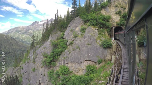 White Pass and Yukon Route Railroad Train Crossing Wooden Bridge Into Dark Tunnel with Majestic Mountain Surroundings