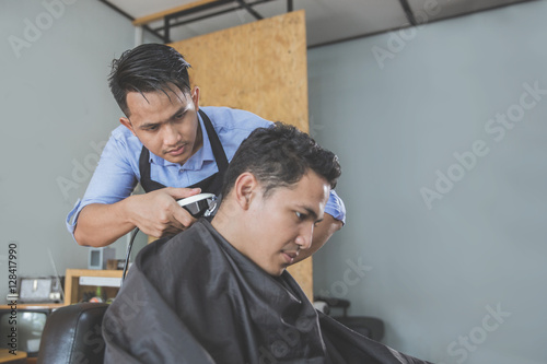 barber making haircut of attractive man in barbershop