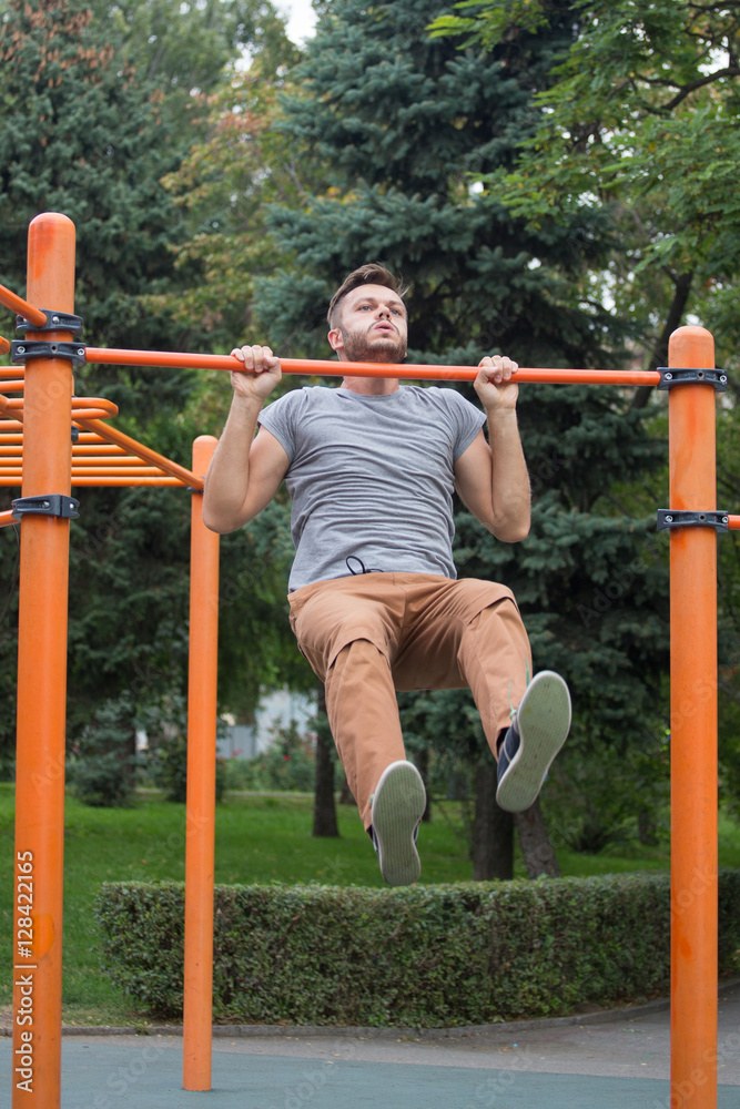Obraz premium young man doing pull ups on horizontal bar outdoors.