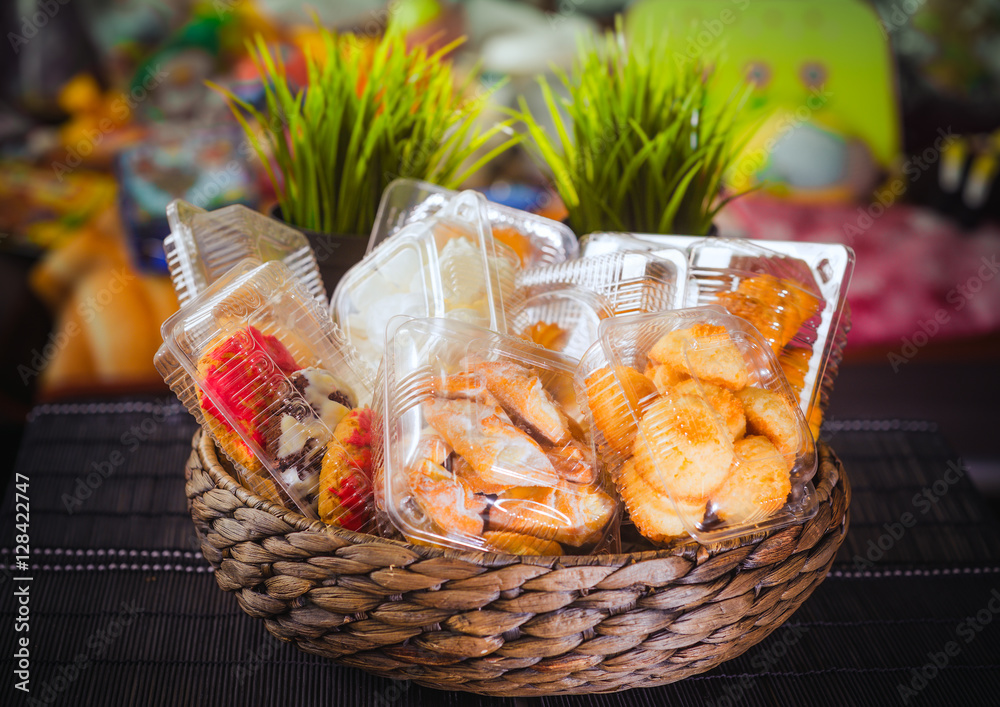 Plastic disposable containers with cookies and pastries in a wicker wooden basket on a motley, colored background Plastic disposable containers with cookies and pastries in a wicker wooden basket on a motley, colored background
