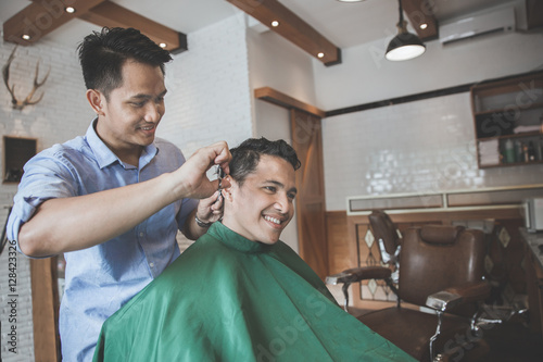 barber making haircut of attractive man in barbershop