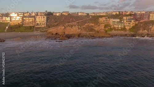 Aerial panning aerial looking toward the beaches and cliff side homes in the Corona Del Mar Neighborhood of Newport Beach, California, during sunset, and wind driven surf during a winter weekend