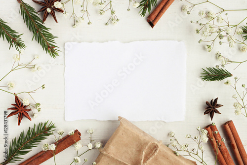 Empty congratulation note framed natural wintertime decor elements. Green pine twigs, cinnamon sticks, craft gift box, white background.