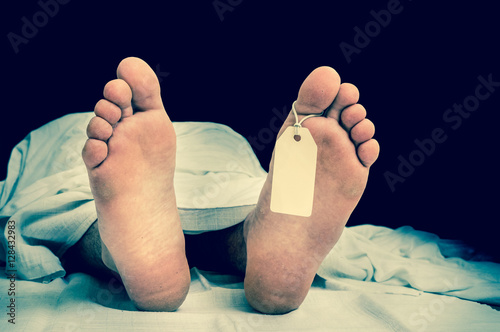 The dead man's body with blank tag on feet under white cloth photo