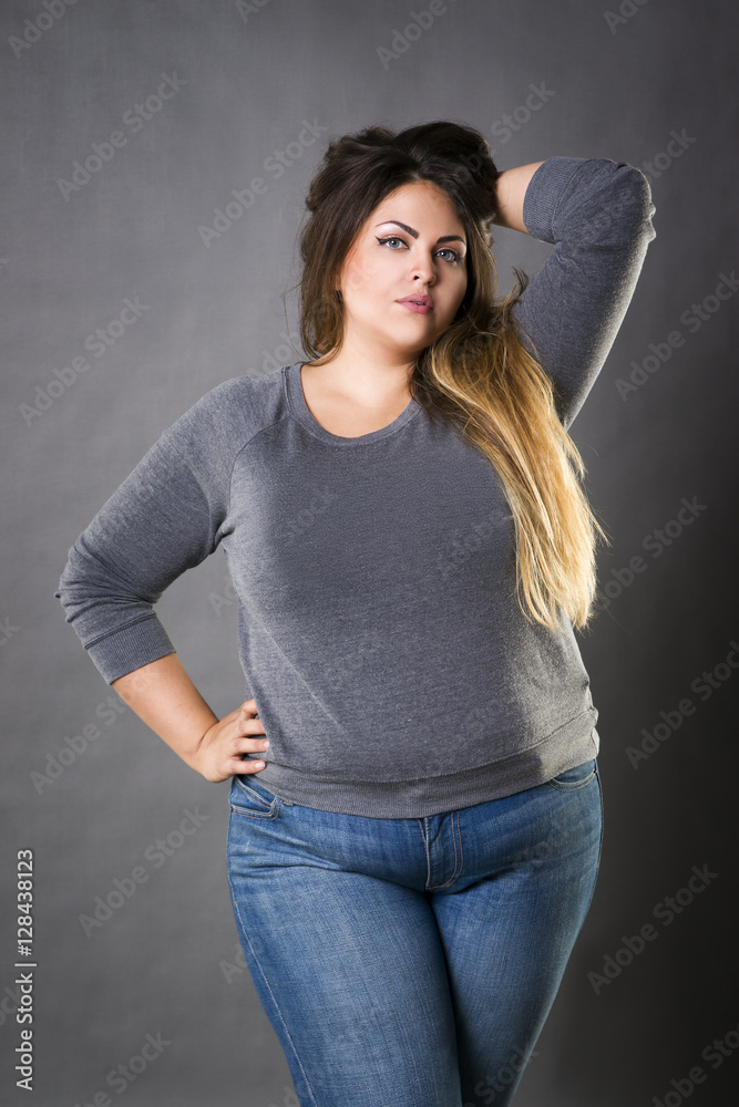 Young beautiful plus size model in blue jeans, xxl woman on gray background  Stock Photo