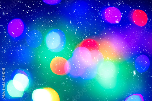 Defocused colorful ligths of Christmas tree. Multicolored bokeh lights during a snowfall. Background for greeting card. Winter composition. Happy holiday mood. Xmas and New Year fairy tale wallpaper.