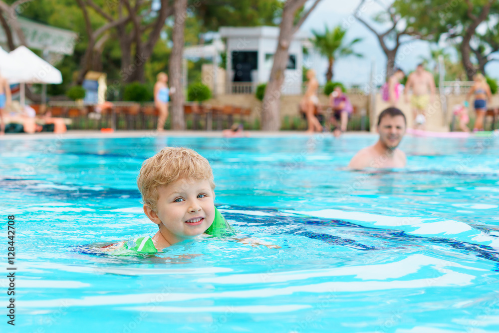 Little blond kid learning to swim in the resort pool. Dressed inflatable armbands. Watching instructor on a blurred background.