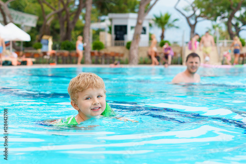 Little blond kid learning to swim in the resort pool. Dressed inflatable armbands. Watching instructor on a blurred background. © Denys