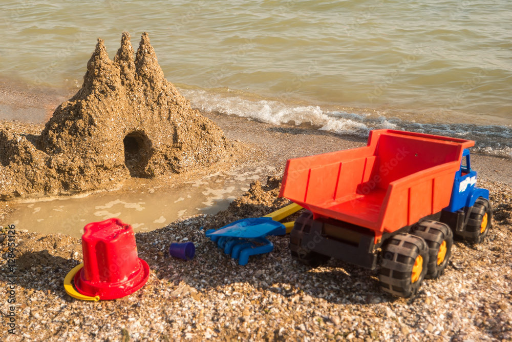 Sandcastle on the shore. Toy truck on sand. Turn on your imagination. Dig and build. Sandcastle on the shore. Toy truck on sand. Turn on your imagination. Dig and build.