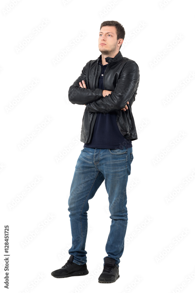 Serious young casual man in leather jacket and jeans with crossed arms looking away. Full body length portrait isolated over white studio background. Serious young casual man in leather jacket and jeans with crossed arms looking away. Full body length portrait isolated over white studio background.