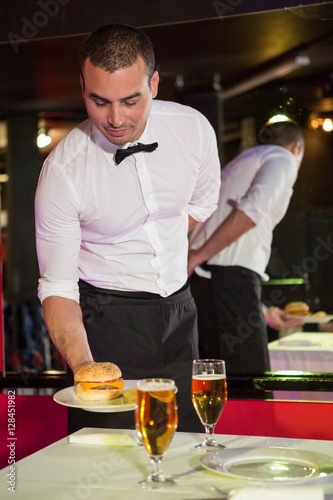 Waiter serving burger and beer on a table