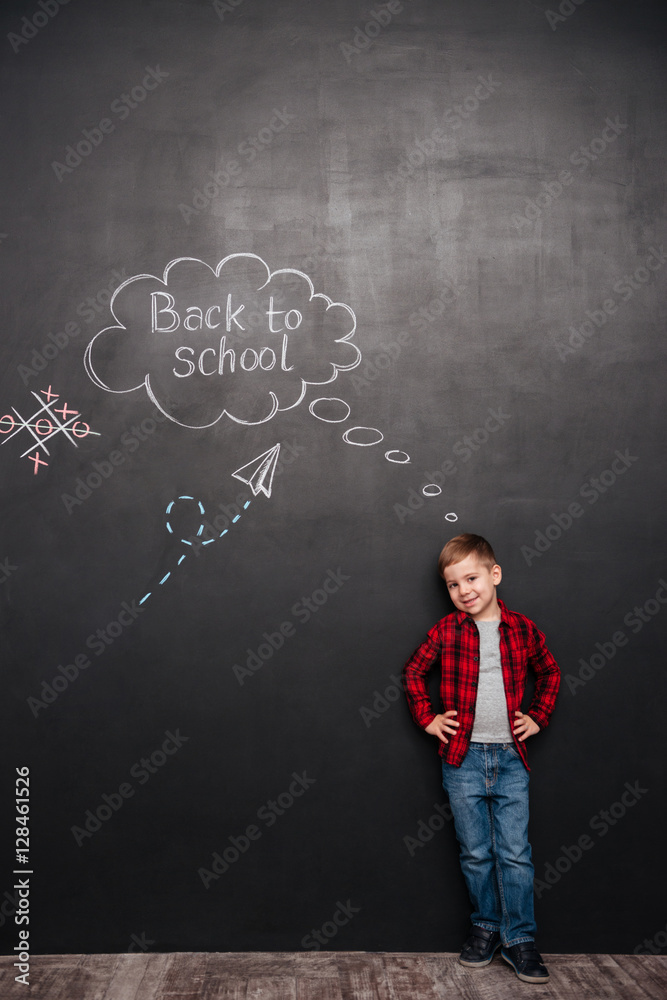 Cute schoolboy standing over background of chalkboard with schoo Cute schoolboy standing over background of chalkboard with schoo