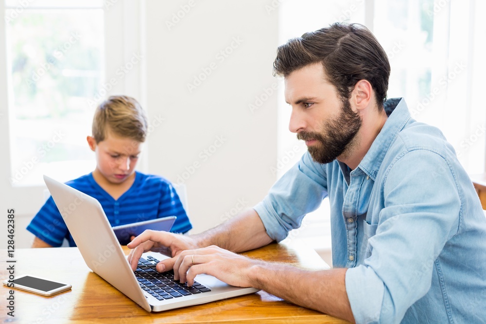 © WavebreakMediaMicro - Father and son using laptop and digital tablet