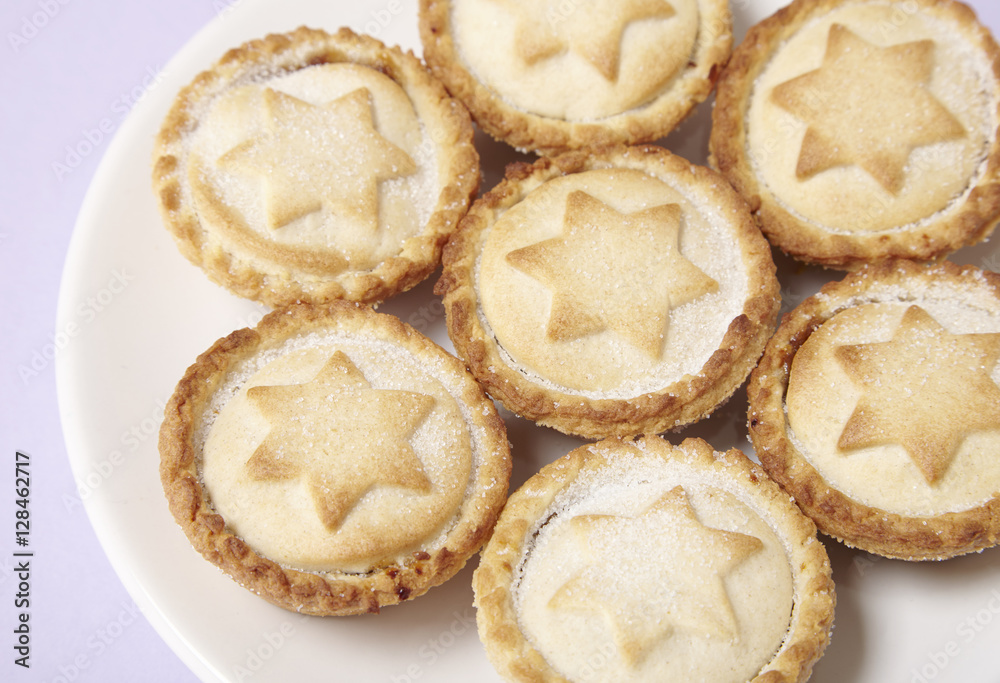 A plate full of freshly baked mince pies on a pastel purple background