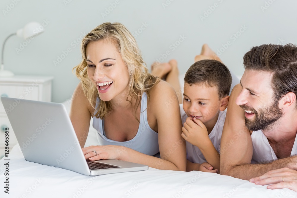 Parents and son lying on bed and using laptop Parents and son lying on bed and using laptop