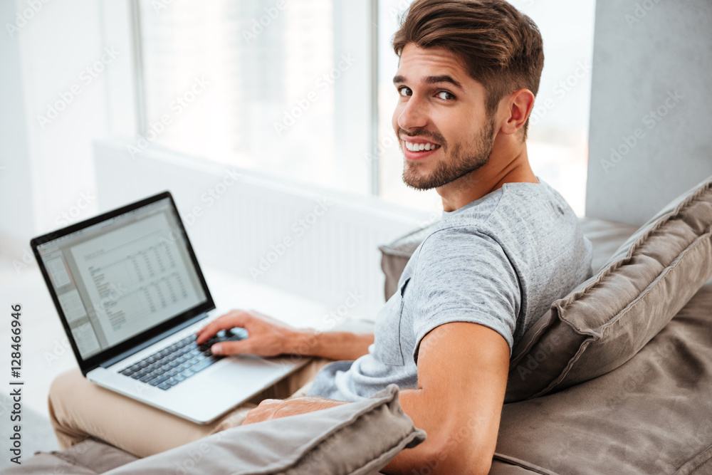 Happy young man sitting with laptop and looking at camera Happy young man sitting with laptop and looking at camera