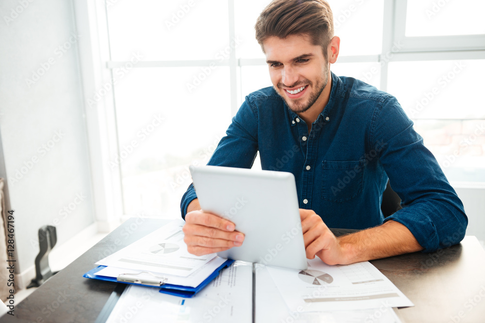 Happy young man analyzing finances at home and holding tablet Happy young man analyzing finances at home and holding tablet