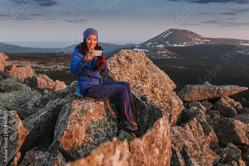 woman hiker with smart phone at mountain peak cliff at the sunset photo