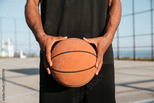 Portrait of male hands holding basketball with playground on background