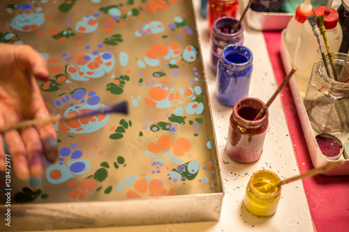 Traditional Turkish art Ebru in process. Woman hand sprinkling paint over water and colourful paint bottles standing next to the ebru tray