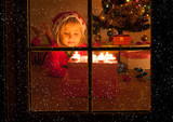 happy cheerful little girl blowing candles at Christmas, view from outside window