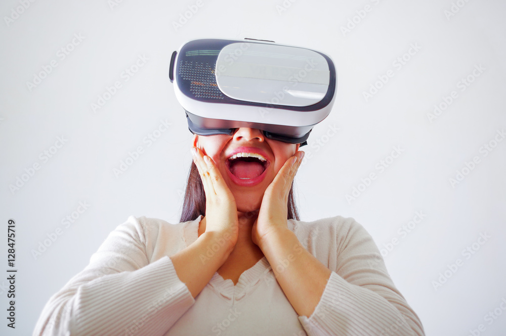 Young brunette woman wearing virtual reality goggles experiencing future technology, interacting and smiling while playing, studio background, vr concept Young brunette woman wearing virtual reality goggles experiencing future technology, interacting and smiling while playing, studio background, vr concept