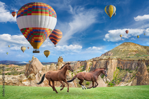 Hot air ballooning and two horses running in Cappadocia, Turkey.