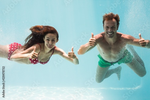 Smiling couple showing thumbs up while swimming  #128478732
