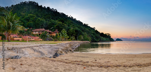 View of tropical hotel beach among the palm trees, beautiful lawn and benches at sunset. Beach sunset is a golden sunset sky with a wave rolling to shore