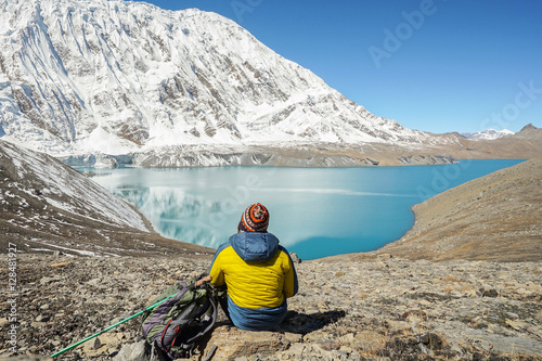Travel concept: Trekker with tourist sticks and backpack on Tilicho lake. Its 4900m above sea level. Snowly peaks of mountains and Tilicho lake on background. photo