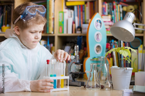 Cute school kid boy sitting at the table making science experiments at home. Learning activities with children at home. Doing water tests. Future profession - scientist.