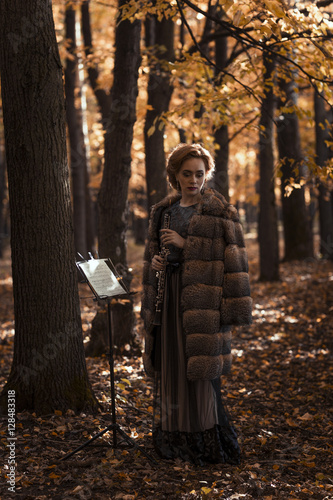 Young attractive woman holding oboe standing against musical stand in fall park