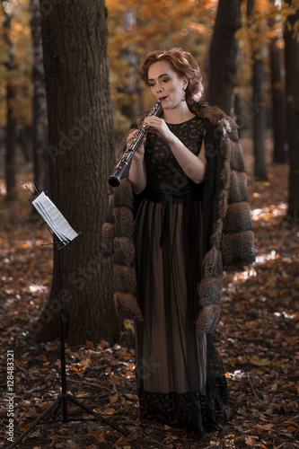 Young woman oboist playing in fall park