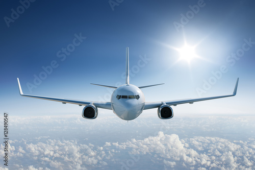 Airplane flying above the clouds  towards the camera with the sun in blue sky